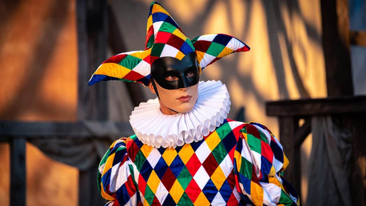 Arlecchino in costume tradizionale a rombi colorati su sfondo teatrale