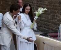 Damiano David in doppiopetto color panna apre la portiera della Lancia d'epoca color crema a Dove Cameron, in tailleur bianco con un mazzo di calle, all'arrivo al Palazzo Comunale di Montalcino