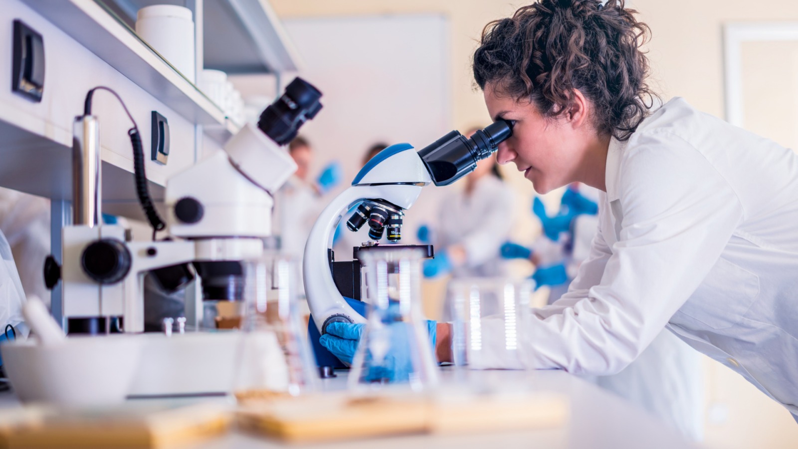 Ricercatrice in camice bianco osserva al microscopio in un laboratorio scientifico