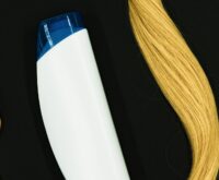 Caduta dei capelli in autunno: una spazzola di legno, un flacone di shampoo e una ciocca di capelli biondi su fondo nero