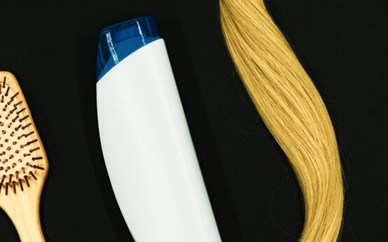 Caduta dei capelli in autunno: una spazzola di legno, un flacone di shampoo e una ciocca di capelli biondi su fondo nero