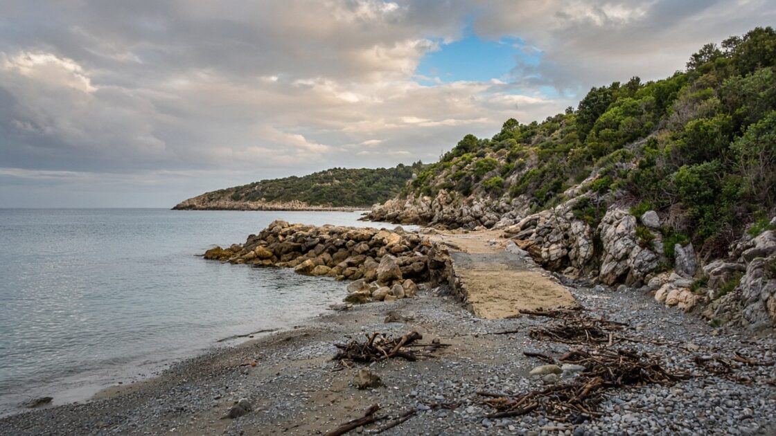Illustrazione del tema: una spiaggia generica di ghiaia con rami e detriti davanti a un piccolo molo, su una costa rocciosa dopo un temporale. Non è la spiaggia nuova a Patresi (immagine generata con IA, a scopo illustrativo)
