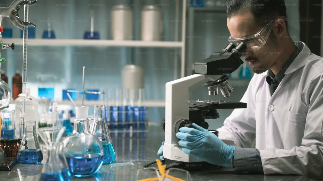 Ricercatore in camice e guanti osserva un campione al microscopio in un laboratorio, foto di repertorio