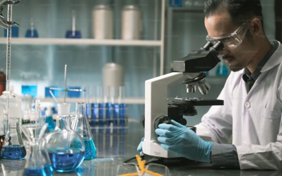 Ricercatore in camice e guanti osserva un campione al microscopio in un laboratorio, foto di repertorio