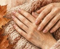 Illustrazione generata con AI: mani con unghie corte e lucide su una coperta di lana, con foglie autunnali