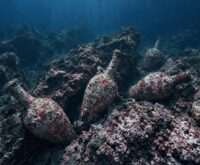 Illustrazione generata con AI: anfore romane ricoperte di concrezioni rosa incastrate tra le rocce di un fondale marino profondo