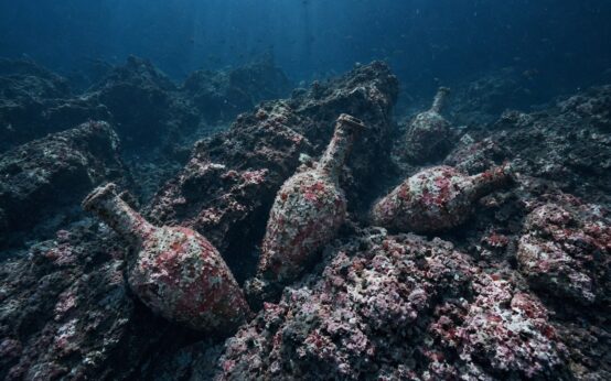 Illustrazione generata con AI: anfore romane ricoperte di concrezioni rosa incastrate tra le rocce di un fondale marino profondo