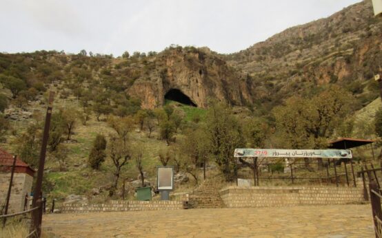 L'ingresso della grotta di Shanidar, sui monti Bradost nel Kurdistan iracheno, visto dal piazzale d'accesso tra alberi e pareti di roccia