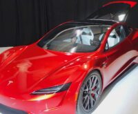 Prototipo rosso della Tesla Roadster di seconda generazione esposto su una pedana bianca, con il tetto aperto