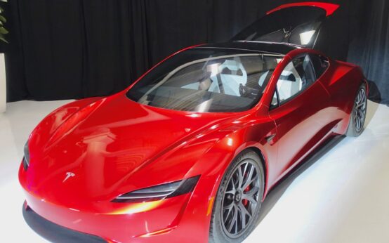 Prototipo rosso della Tesla Roadster di seconda generazione esposto su una pedana bianca, con il tetto aperto