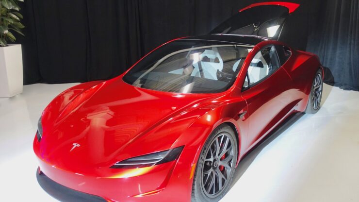 Prototipo rosso della Tesla Roadster di seconda generazione esposto su una pedana bianca, con il tetto aperto